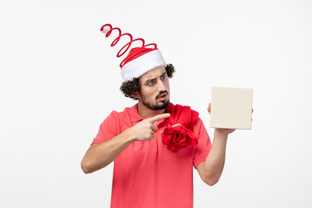 Вид спереди молодого человека, держащего праздничный подарок на белой стене