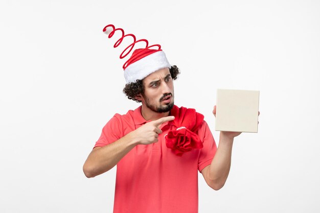 Front view of young man holding holiday present on white wall