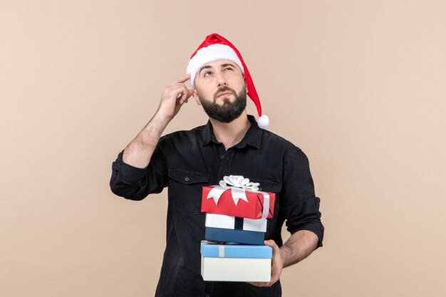 Front view of young man holding holiday presents on a pink wall