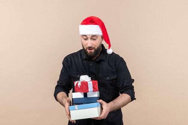 Front view of young man holding holiday presents on pink wall