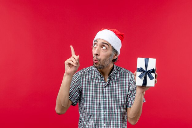 Front view of young man holding little present on red