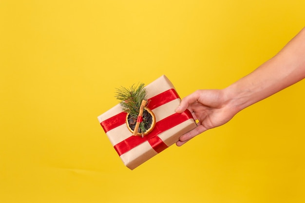 Front view of young man holding little xmas present on yellow wall