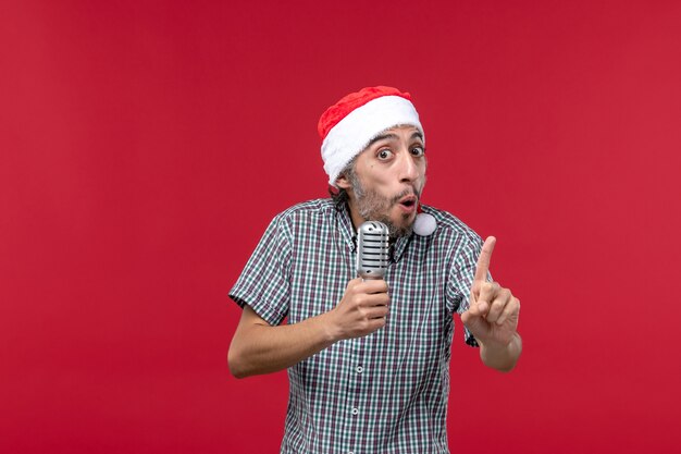 Вид спереди молодой человек держит микрофон на красной стене эмоции праздник певица музыка