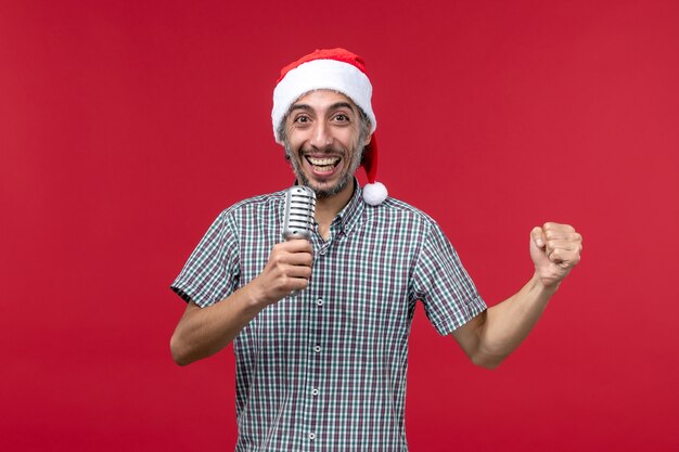 Вид спереди молодой человек, держащий микрофон на красной стене эмоция праздничная музыкальная певица