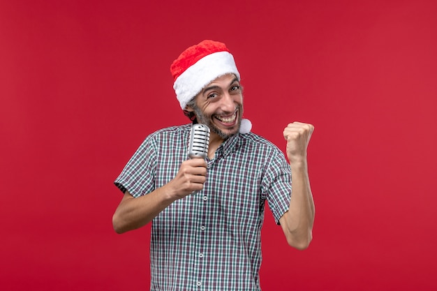 Вид спереди молодой человек, держащий микрофон на красной стене эмоция праздничная музыкальная певица