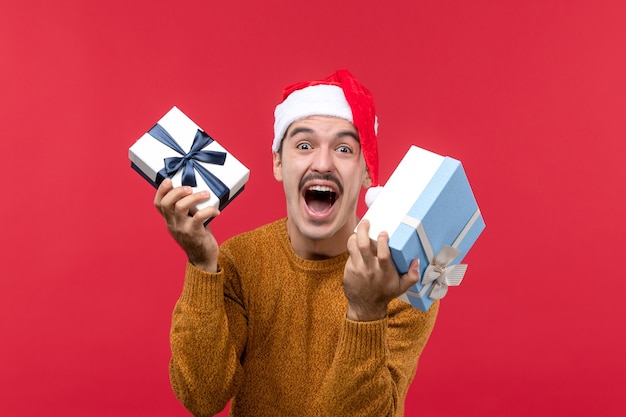 Front view of young man holding new year presents on a red wall