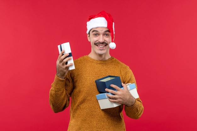 Front view of young man holding new year presents on a red wall