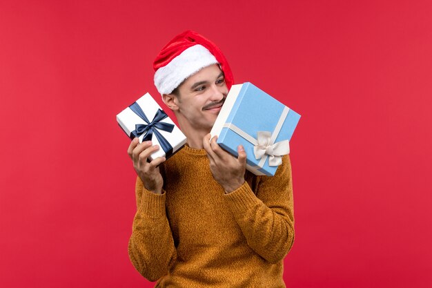 Front view of young man holding new year presents on red wall