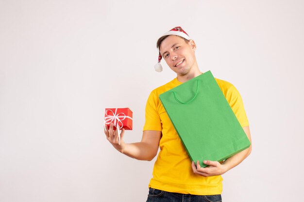 Front view of young man holding package and little present on white wall