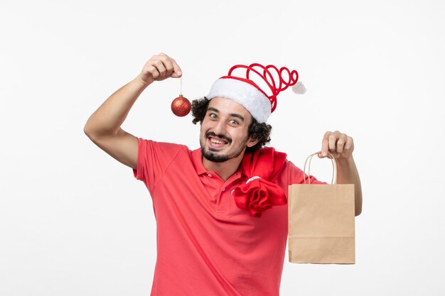 Front view of young man holding package with present on a white wall