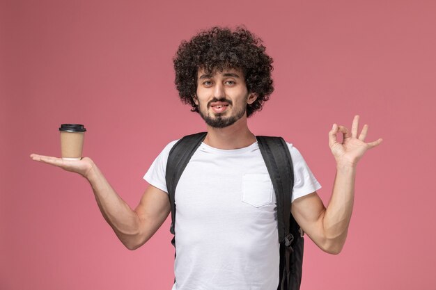 Front view young man holding paper coffee cup in his hand and showing ok gesture