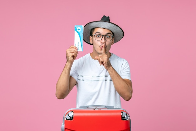 Front view of young man holding plane ticket on pink wall