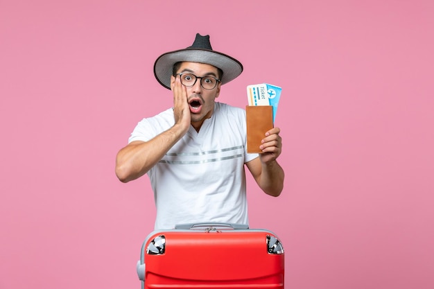 Front view of young man holding plane tickets preparing for vacation on pink wall