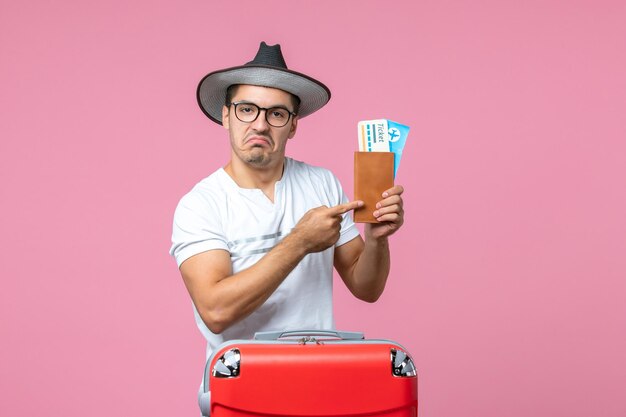 Front view of young man holding plane tickets preparing for vacation on pink wall