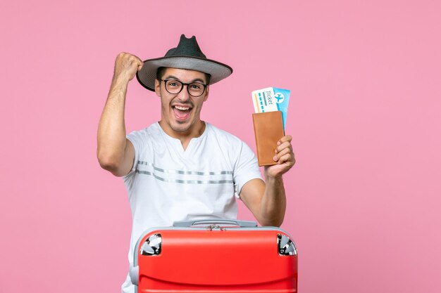 Front view of young man holding plane tickets preparing for vacation on pink wall