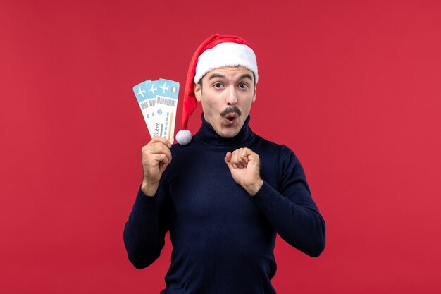 Front view young man holding plane tickets on red background