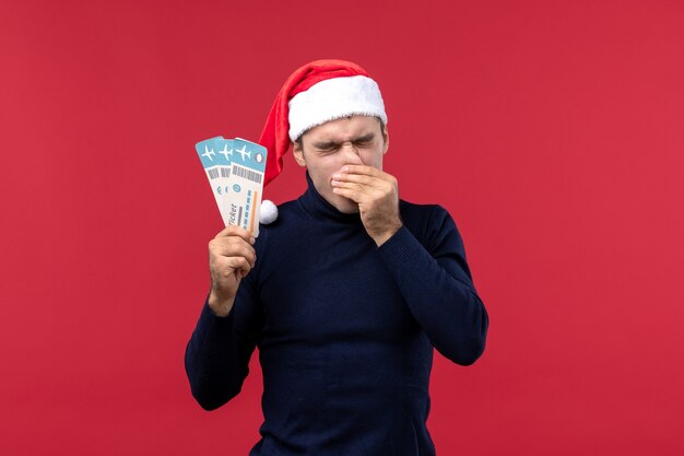 Front view young man holding plane tickets on red desk