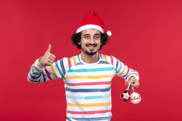 Front view young man holding plastic toys on red wall holiday new year red human