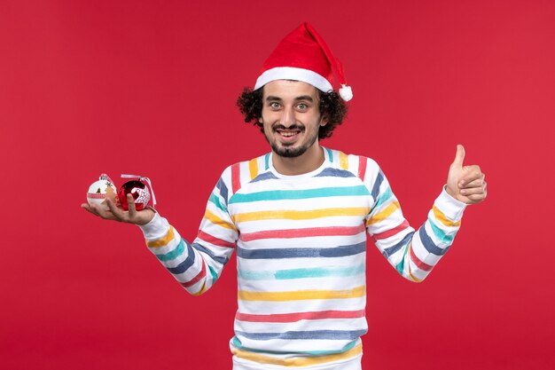 Вид спереди молодой человек с пластиковыми игрушками на красной стене красные люди новогодний праздник