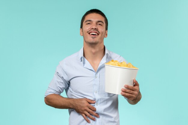 Front view young man holding potato cips on a blue floor lonely remote male movie cinema