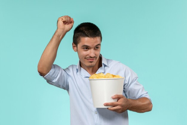 Молодой человек, держащий картофельные чипсы и танцующий на синей стене, одинокий удаленный мужской кинотеатр, вид спереди