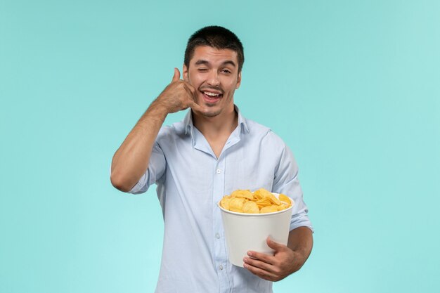 Front view young man holding potato cips and posing on a blue wall lonely remote male movie cinema