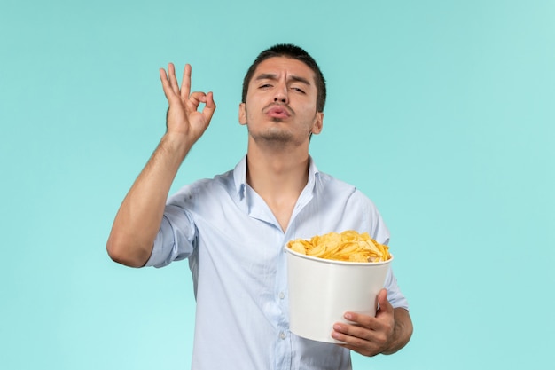 Front view young man holding potato cips posing on a blue wall lonely remote male movie cinema