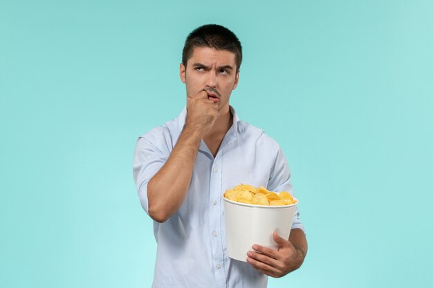 Front view young man holding potato cips and thinking on a blue wall lonely remote male movie cinema