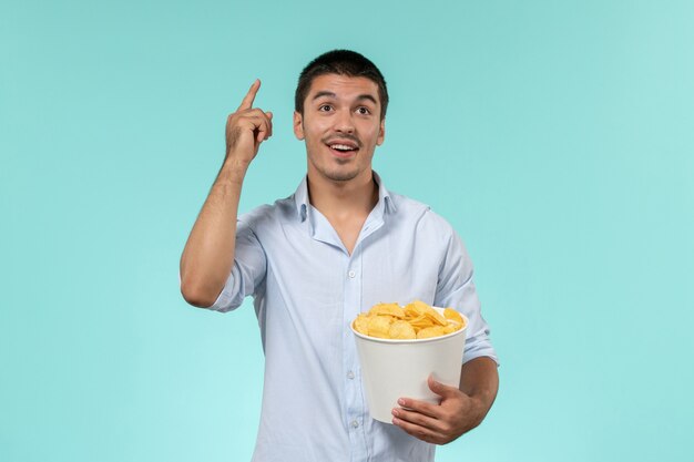 Вид спереди молодой человек держит картофельные чипсы и думает на синей стене одинокий удаленный мужской кинотеатр