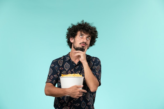 Front view young man holding potato cips and thinking on blue wall male cinema movie film theater