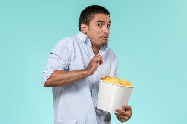 Front view young man holding potato cips and watching movie on blue wall lonely remote movie cinema