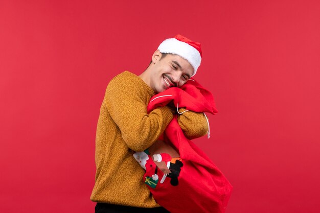 Free photo front view of young man holding present bag on red wall