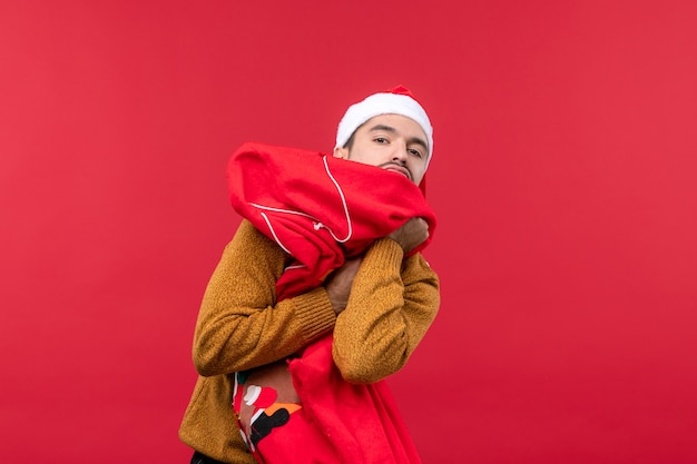 Front view of young man holding present bag on red wall