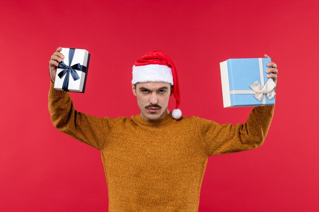 Front view of young man holding present boxes on red wall