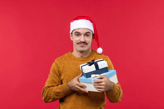 赤い壁にプレゼントボックスを保持している若い男の正面図