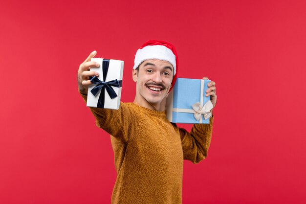 Front view of young man holding present boxes on red wall