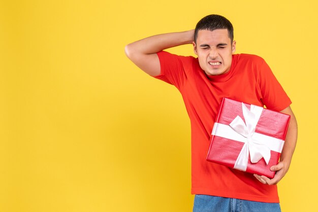 Front view of young man holding present having headache on yellow wall