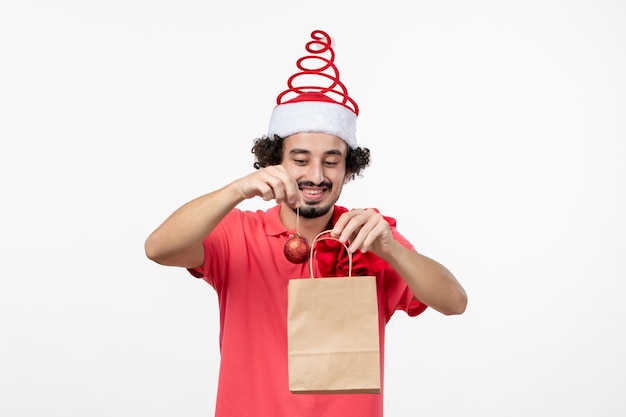 Front view of young man holding present in package on white wall