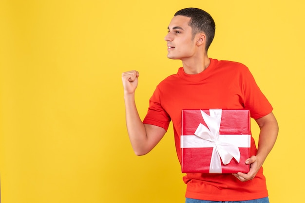 Front view of young man holding present rejoicing on yellow wall