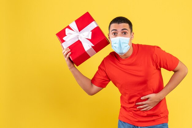 Front view of young man holding present in sterile mask on a yellow wall