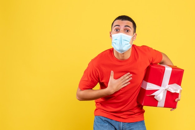 Front view of young man holding present in sterile mask on yellow wall