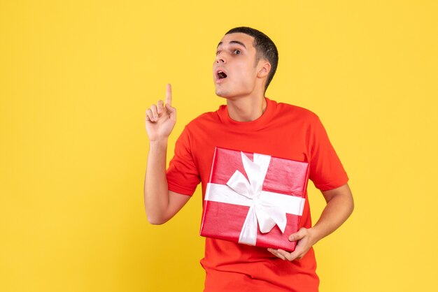 Front view of young man holding present surprised on yellow wall