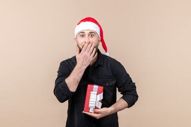 Front view of young man holding present with shocked face on pink wall