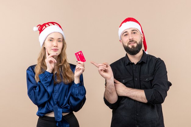 Front view of young man holding present with woman who's holding bank card on pink wall