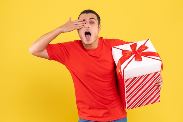 Free photo front view of young man holding present on a yellow wall