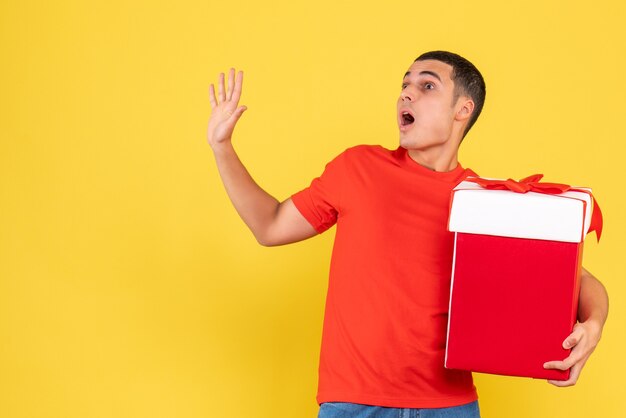 Front view of young man holding present on yellow wall