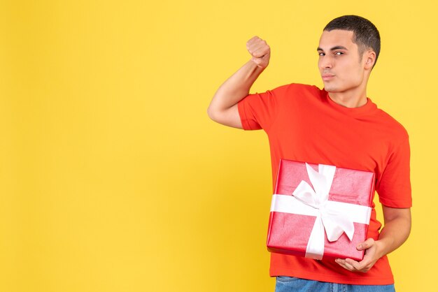 Front view of young man holding present on yellow wall