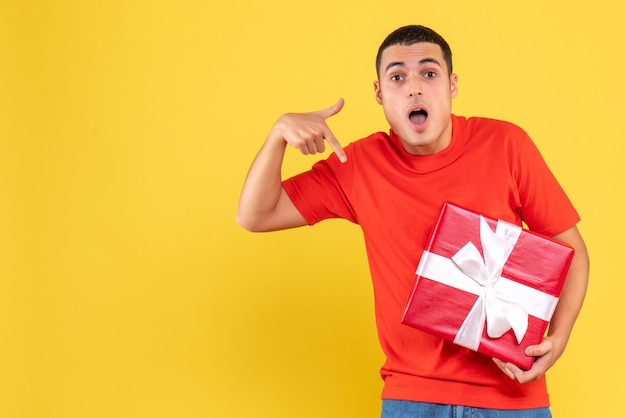 Front view of young man holding present on yellow wall