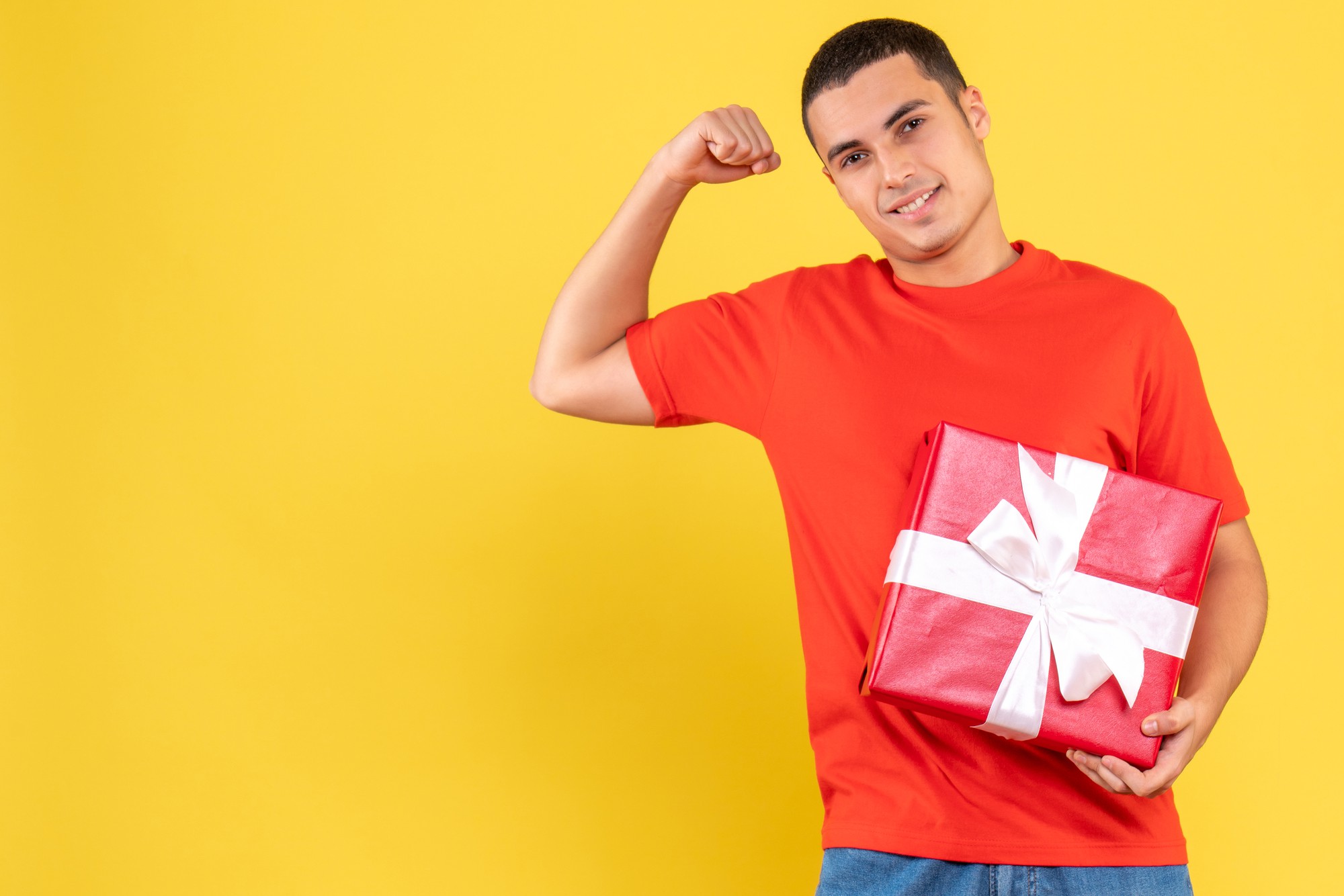 Front view of young man holding present on yellow wall