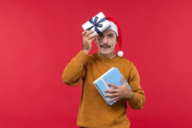 Front view of young man holding presents on a red wall